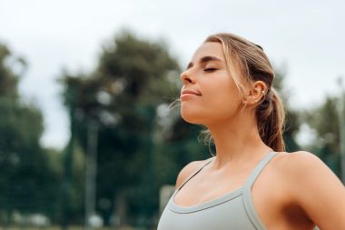 Portrait of smiling, beautiful, young woman breathe with closed eyes on the street, outdoors after training, copy space. Sport, motivation concept